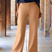 A person wearing wide-leg tan pants, paired with a navy long-sleeve top and black shoes, standing in a stone corridor.
