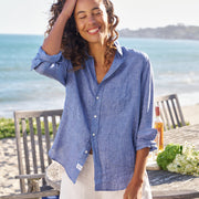 Woman wearing a blue shirt and white pants standing on a beach with ocean view.