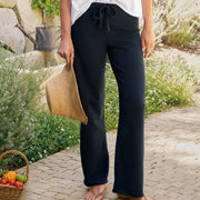Woman in white top and navy pants standing outdoors with a basket of fruit and straw hat.