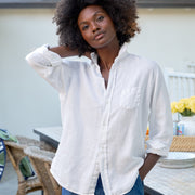 Woman in a white shirt and blue shorts standing outdoors near a dining table with yellow flowers.