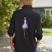 Person wearing a black shirt with a white graphic on the back, standing outdoors.