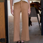 A person wearing tan wide-leg cropped pants with a cream long-sleeve top and dark brown loafers, standing in a doorway.