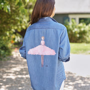 Person wearing a denim shirt with a pink ballerina design outdoors.