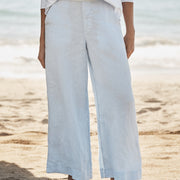 Person wearing light blue wide-leg pants and a white top on a sandy beach.