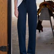 A person wearing dark navy wide-leg drawstring pants, a white long-sleeve top, and brown shoes, standing in a doorway.