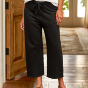 Person wearing black pants and sandals indoors on a wooden floor.