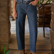 A person wearing barrel-leg blue denim jeans, a white button-up shirt, and brown suede boots, standing on stone steps in a rustic setting.