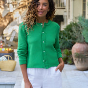 Woman wearing a green cardigan and white pants standing outdoors near a pool.