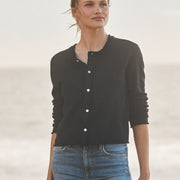 Woman wearing a navy cardigan and blue jeans standing against a light background