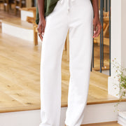 Person wearing white pants and a green top in an indoor setting with wooden flooring.