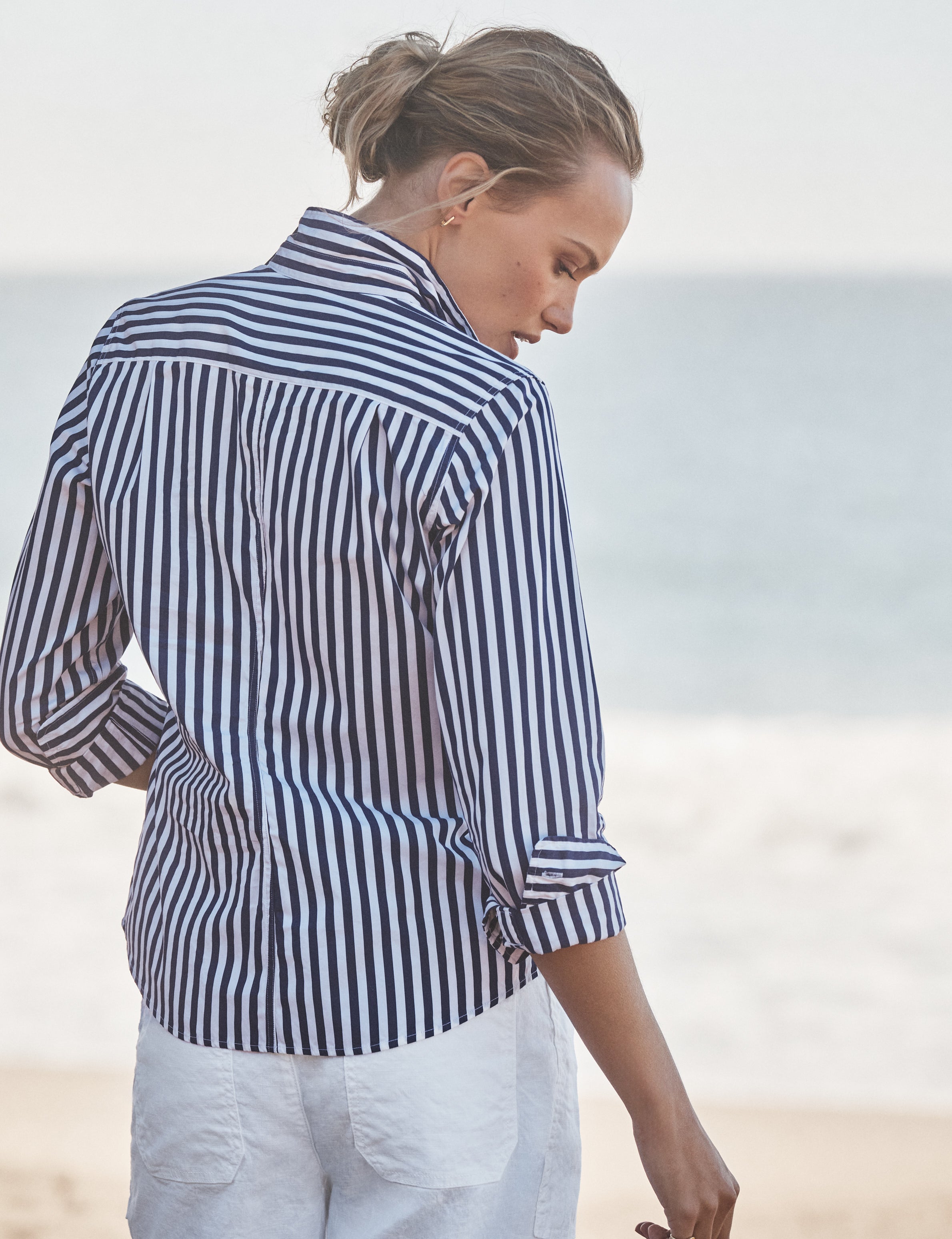 Woman wearing a navy and white striped shirt on a beach, alternate view