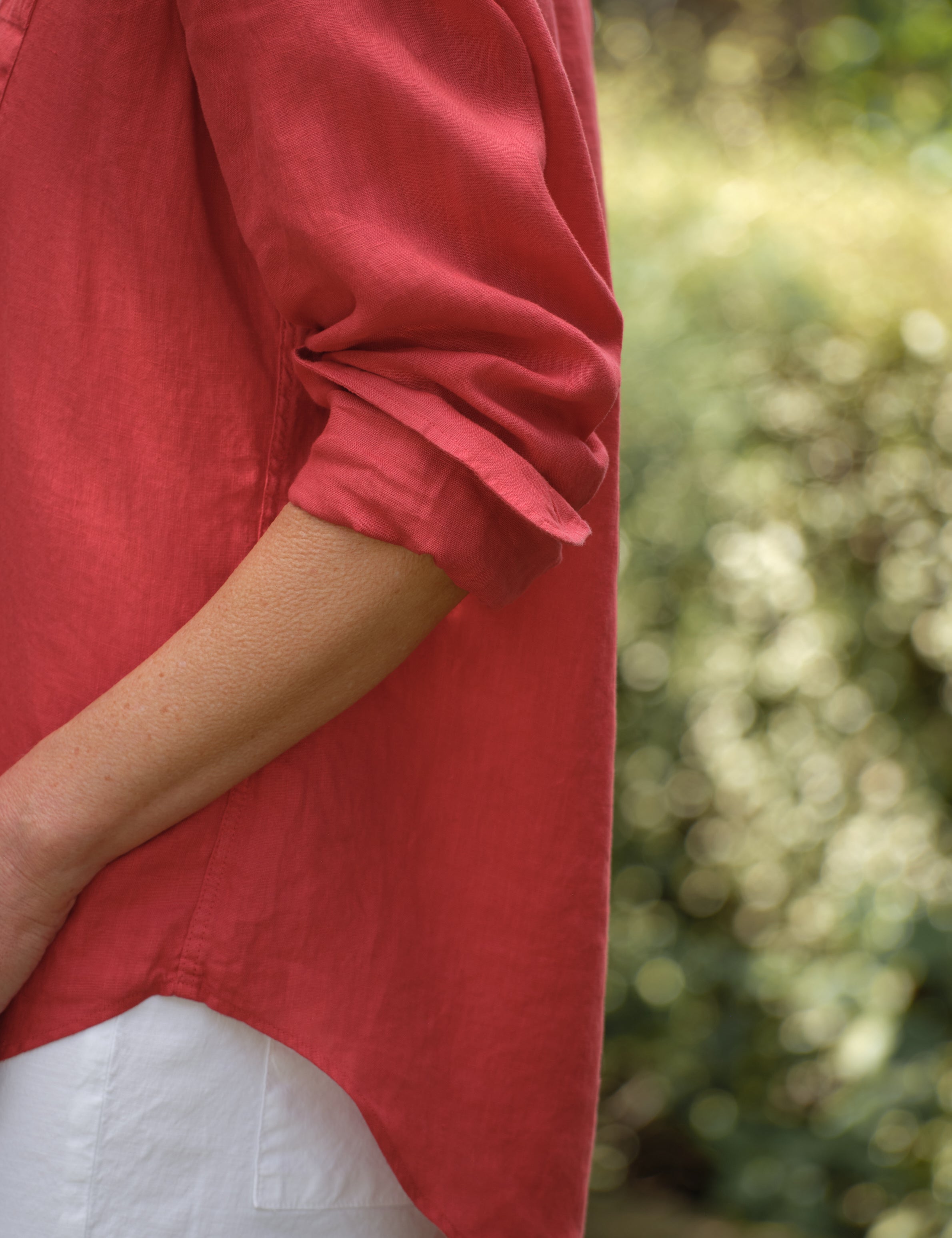 Person wearing a red shirt with rolled-up sleeves against a blurred green background, view 3