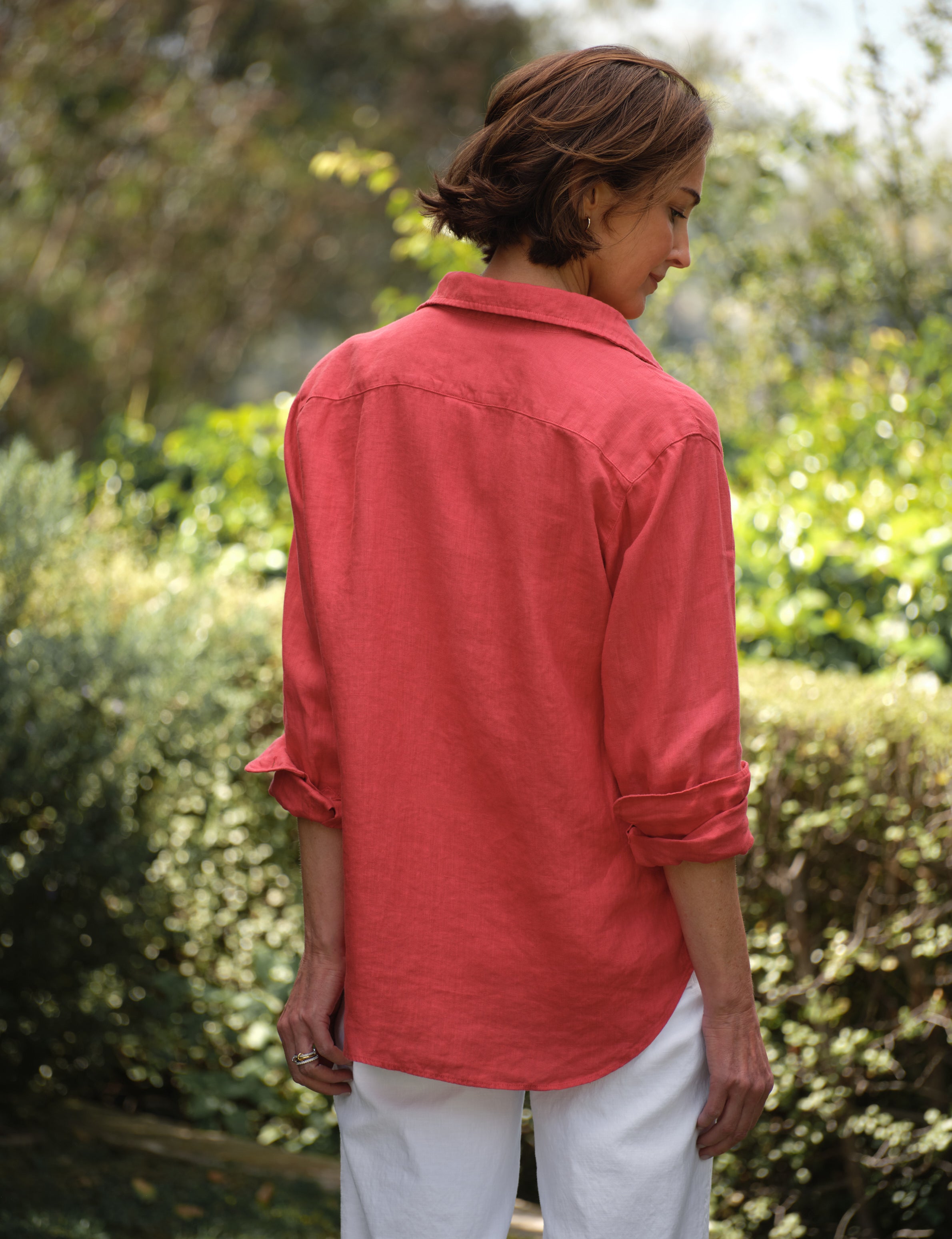 Person wearing a red shirt and white pants standing in a garden, alternate view