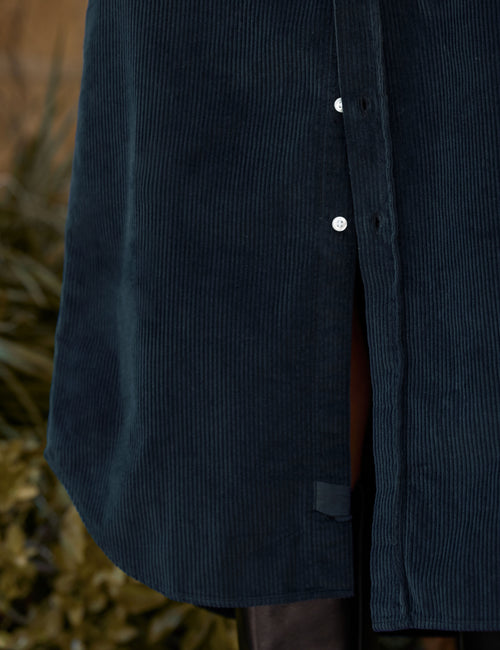 Close-up of a dark navy corduroy button-front garment, showing the ribbed texture, white buttons, and a side slit with a brown lining., view 3