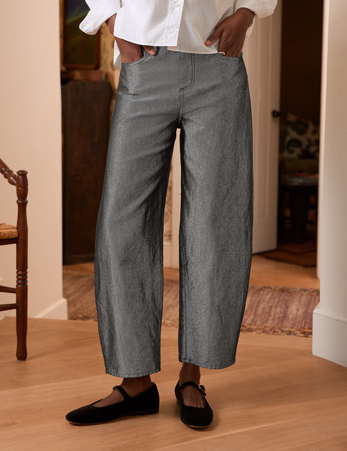 A person wearing gray barrel-leg cropped pants with a white button-up shirt and black flats, standing in a home interior with wood flooring., front view