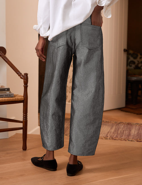 A person shown from the back wearing wide-leg gray textured pants, a white blouse, and black flats in a warm indoor room with wood floors and a chair., alternate view