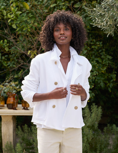 Woman wearing a white jacket with brown buttons outdoors, front view