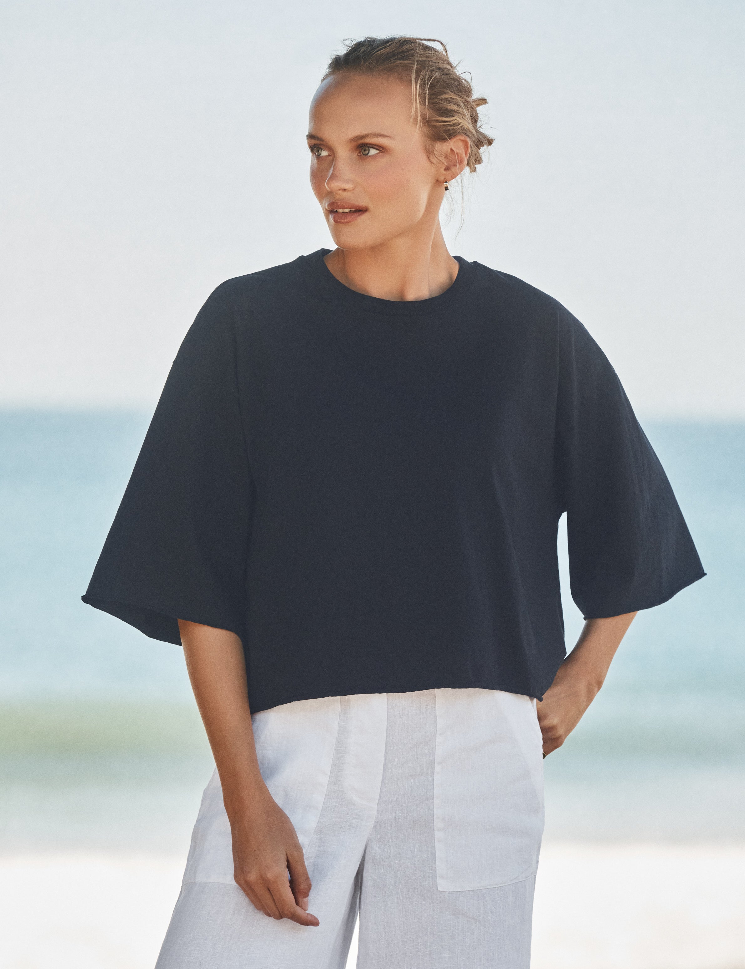 Woman wearing a navy top and white pants against a beach background, front view