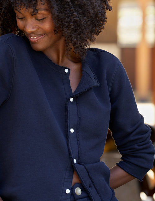 A close-up of a woman wearing a navy blue cardigan with a soft collar, shown in a warm, softly blurred outdoor setting., alternate view