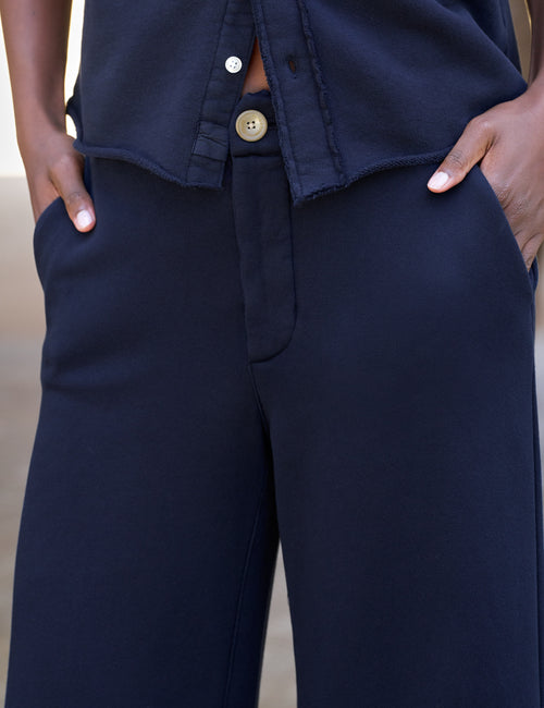 Close-up of a person wearing dark navy wide-leg trousers with hands in the pockets, paired with a matching navy top., view 3
