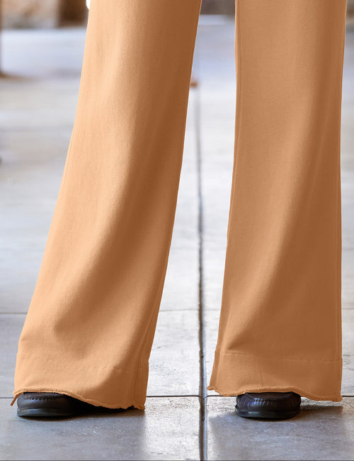 A person wearing high-waisted, wide-leg tan pants with a matching belt, paired with a navy long-sleeve top and black shoes, standing in a stone corridor., view 3