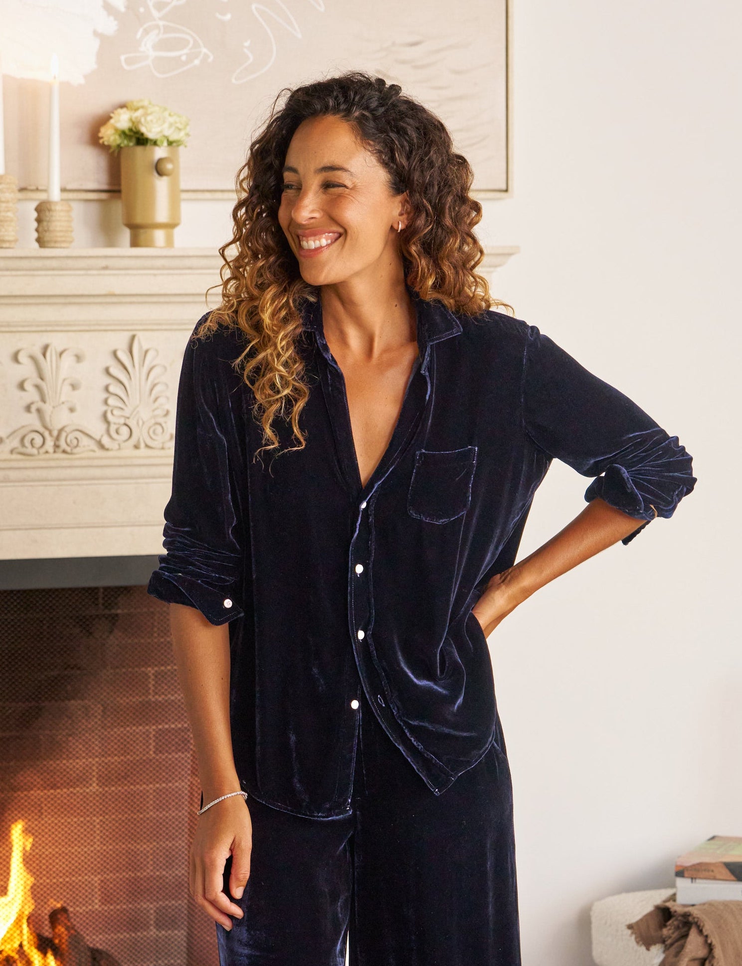 Woman in a navy velvet outfit standing in a cozy living room with a fireplace.