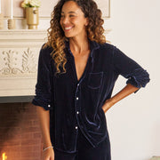 Woman in a navy velvet outfit standing in a cozy living room with a fireplace.