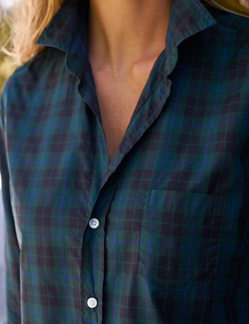 Close-up of a person wearing a dark plaid button-up shirt with a collar and chest pocket. The fabric shows a pattern of deep green, black, and thin blue lines, with white buttons., view 3