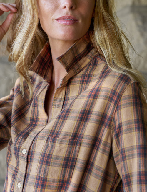 A close-up of a woman wearing a tan and brown plaid button-up shirt with red and yellow stripes, cropped from the mouth down to the waist., view 3