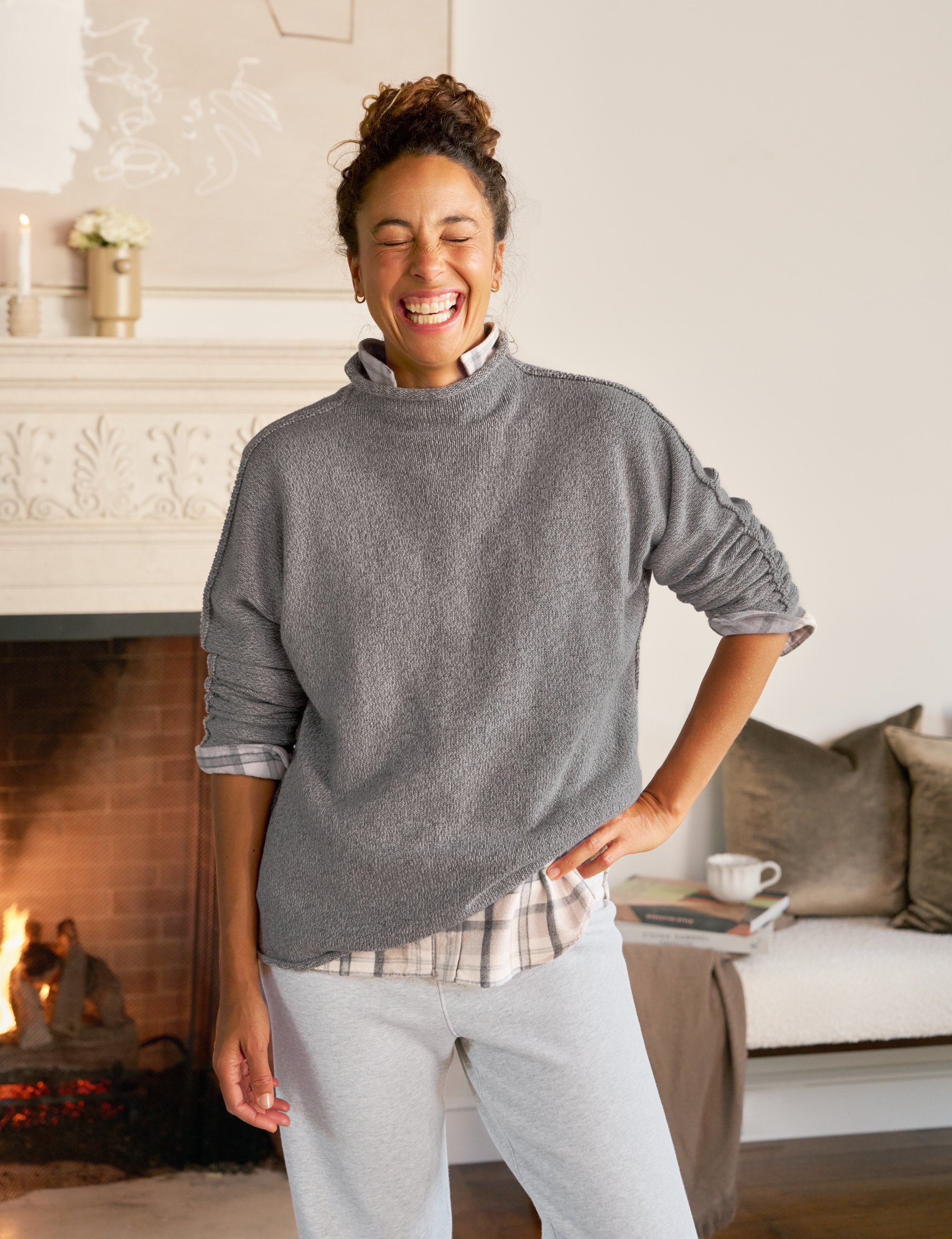 Woman wearing a gray sweater in a cozy living room with a fireplace.