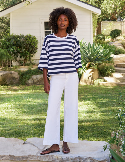 Woman wearing a striped shirt and white pants standing in a garden., view 4