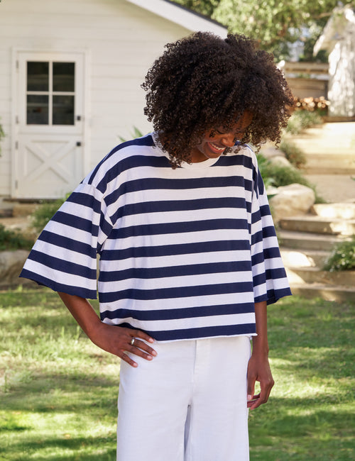 Woman wearing a navy and white striped shirt and white pants standing outdoors., front view