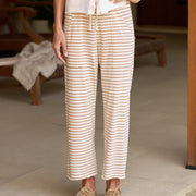 A person wearing cream and tan striped drawstring pants with a white top and tan lace-up shoes, standing indoors on a light stone floor.