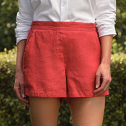 Person wearing red shorts and a white shirt standing on grass with a hedge in the background