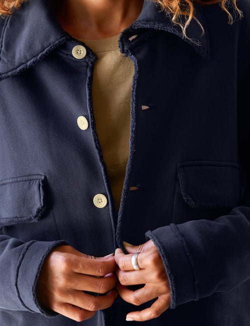 Close-up of a person wearing a dark navy textured jacket with frayed edges, light buttons, and flap pockets over a beige top., view 3