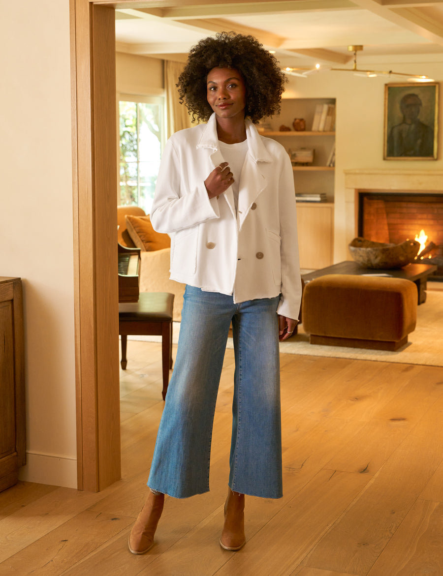 Woman in a white jacket and blue jeans standing in a warm, inviting living room.