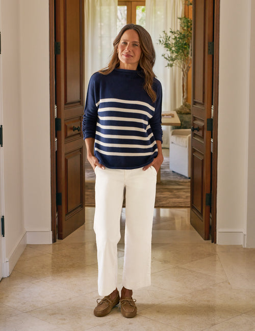Woman wearing a navy and white striped sweater with white pants standing in a home interior., view 3