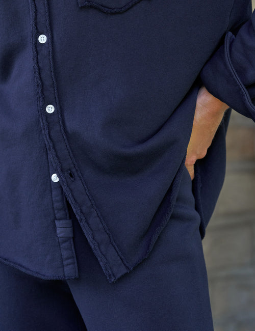 Close-up of a person wearing a dark navy button-front shirt and matching navy pants, with one hand in a pocket. The fabric has a slightly textured, linen-like finish., view 3