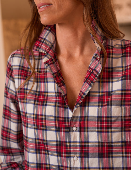 A close-up of a woman wearing a red, white, and navy plaid button-down shirt. The photo focuses on the collar, chest area, and fabric pattern, with the model's hair and neck visible against a softly blurred warm-toned background., view 3