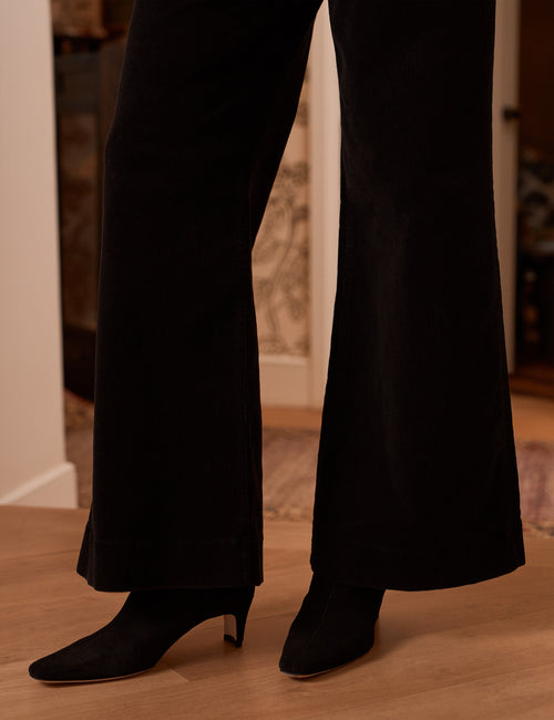 Black wide-leg pants worn with black pointed-toe heeled ankle boots, shown from the knees down on a light wood floor in an indoor setting., view 3