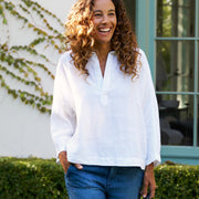Woman in white shirt and blue jeans walking outdoors with a basket, smiling.