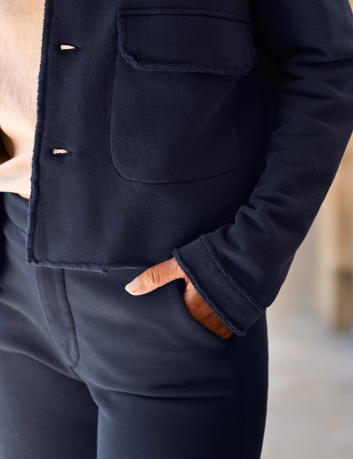 Close-up of a person wearing a dark navy jacket with a large chest pocket and a tan leather patch pocket, paired with matching dark trousers., view 3