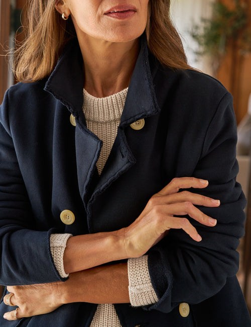 Woman wearing a navy coat with a beige sweater and cuffs, indoors., view 3