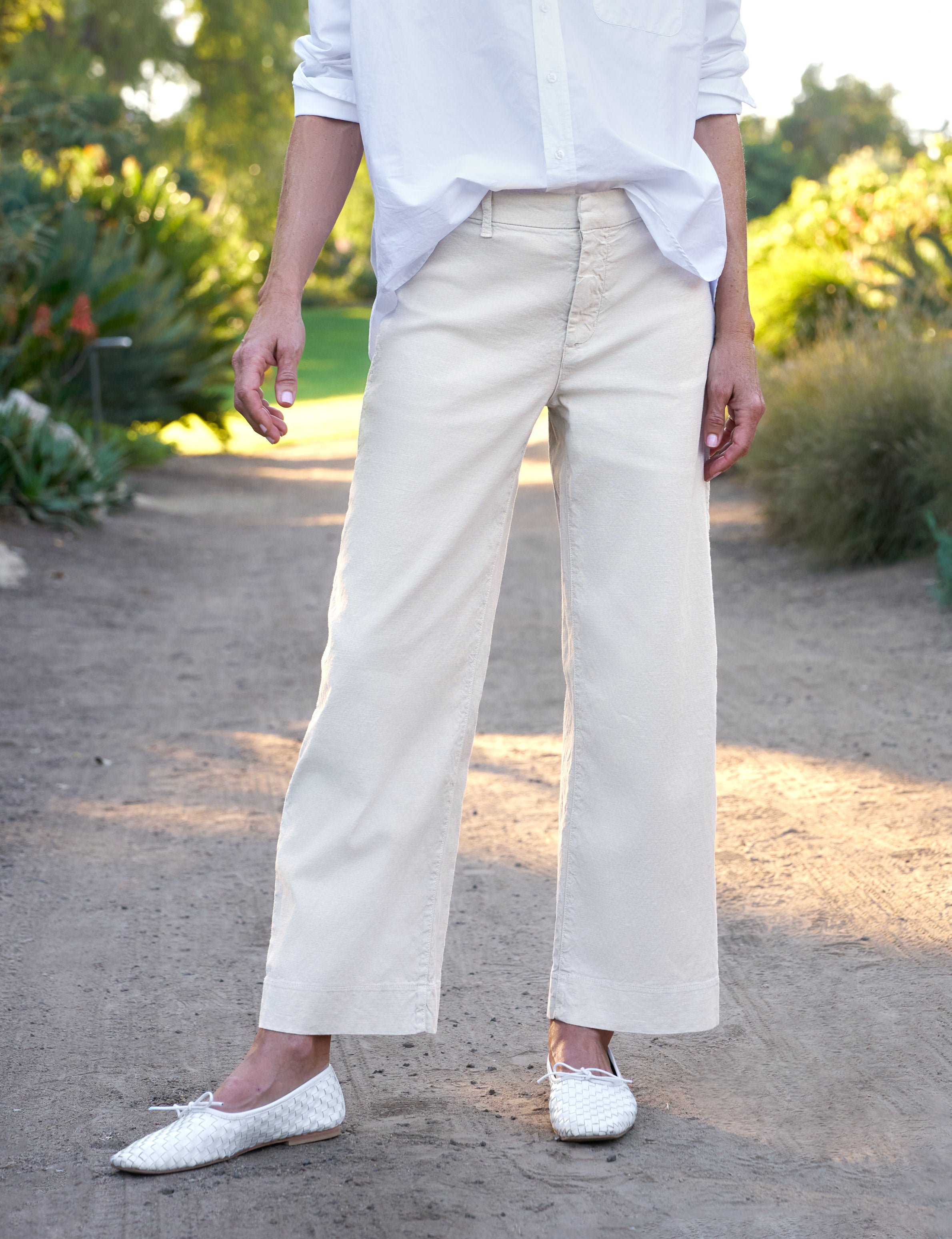 Person wearing beige pants and white shoes in a garden setting, alternate view