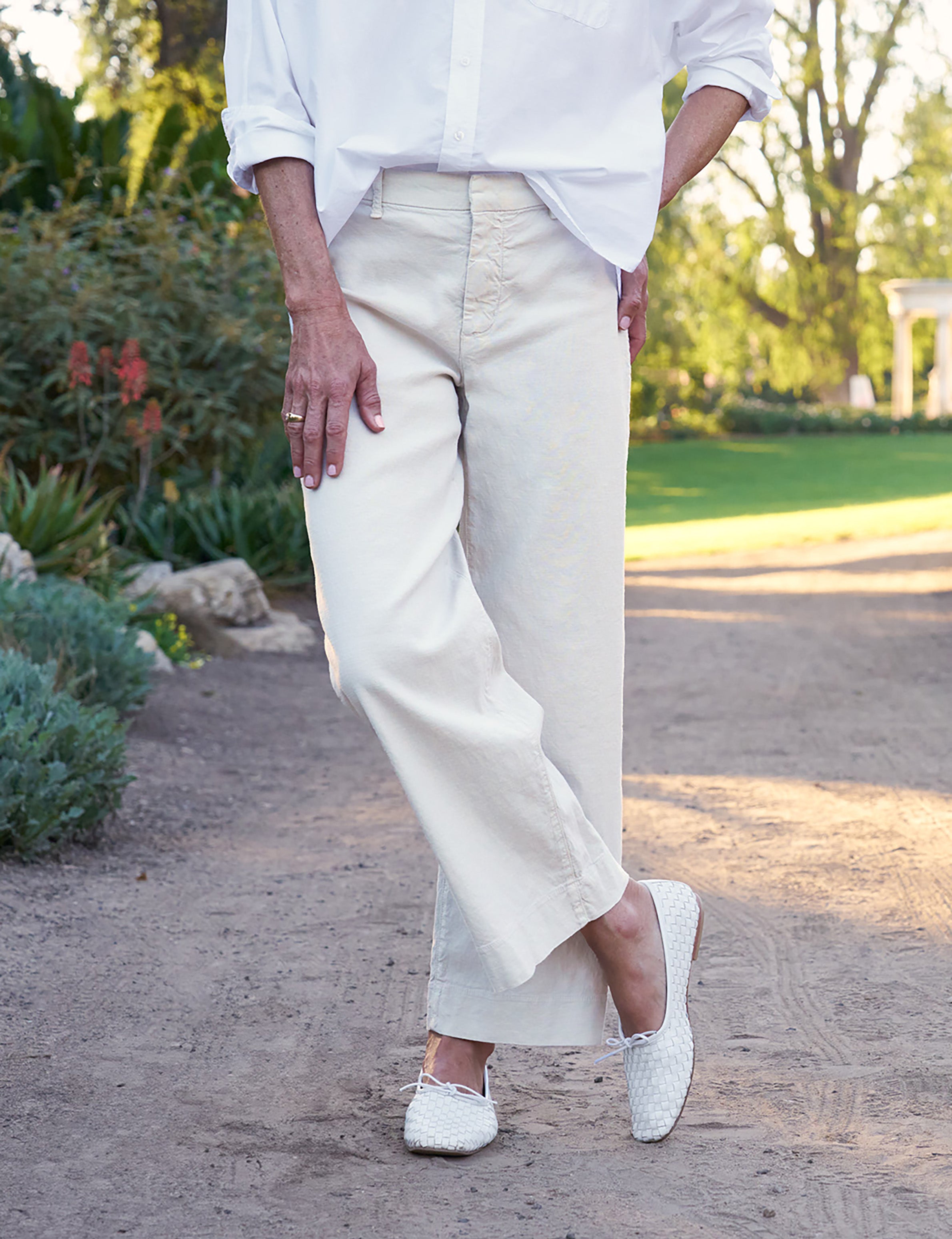 Person wearing a white shirt and beige pants standing outdoors on a path., view 3