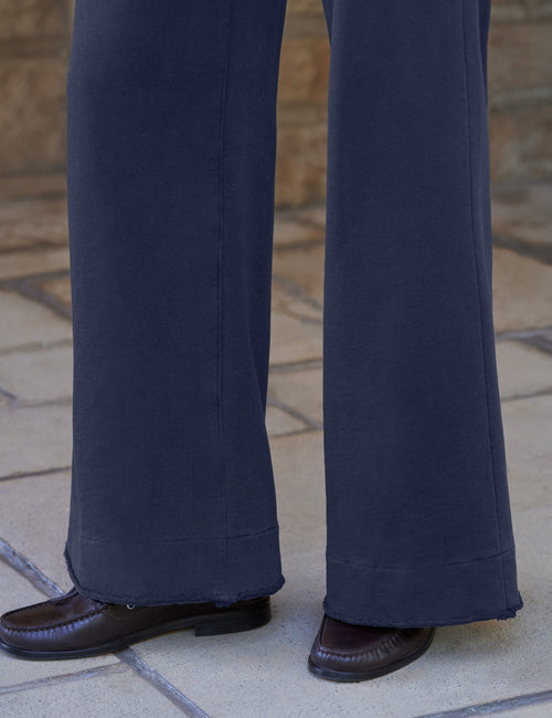 Close-up of a person wearing dark navy wide-leg trousers and dark brown leather loafers, standing on a light stone tiled floor., view 3