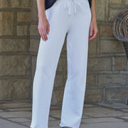 White wide-leg drawstring pants worn by a model standing outdoors against a stone wall.
