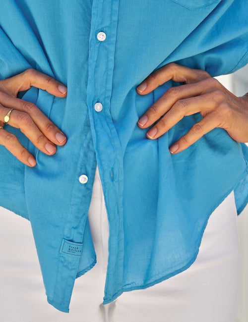 Close-up of a blue shirt with hands adjusting it on a white background, view 3