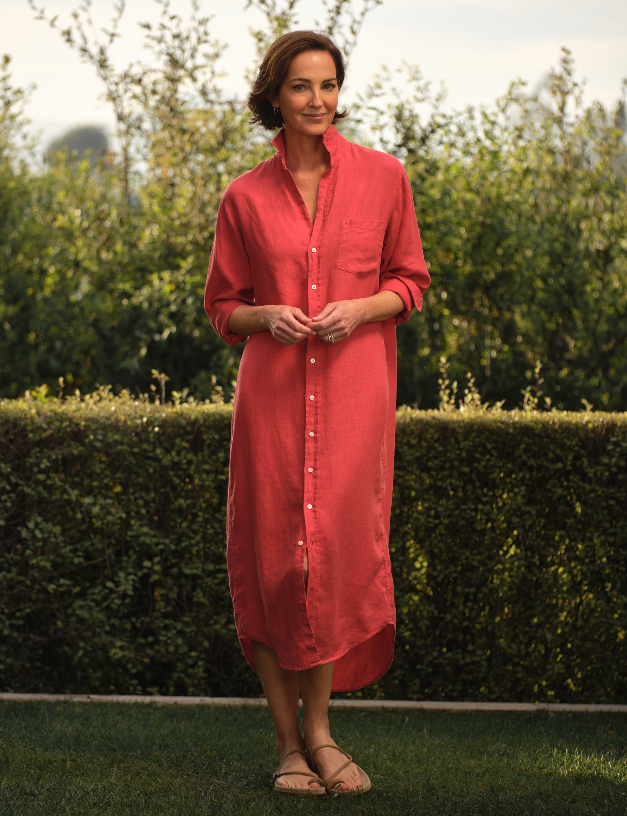 Woman wearing a red dress standing outdoors with greenery in the background, front view
