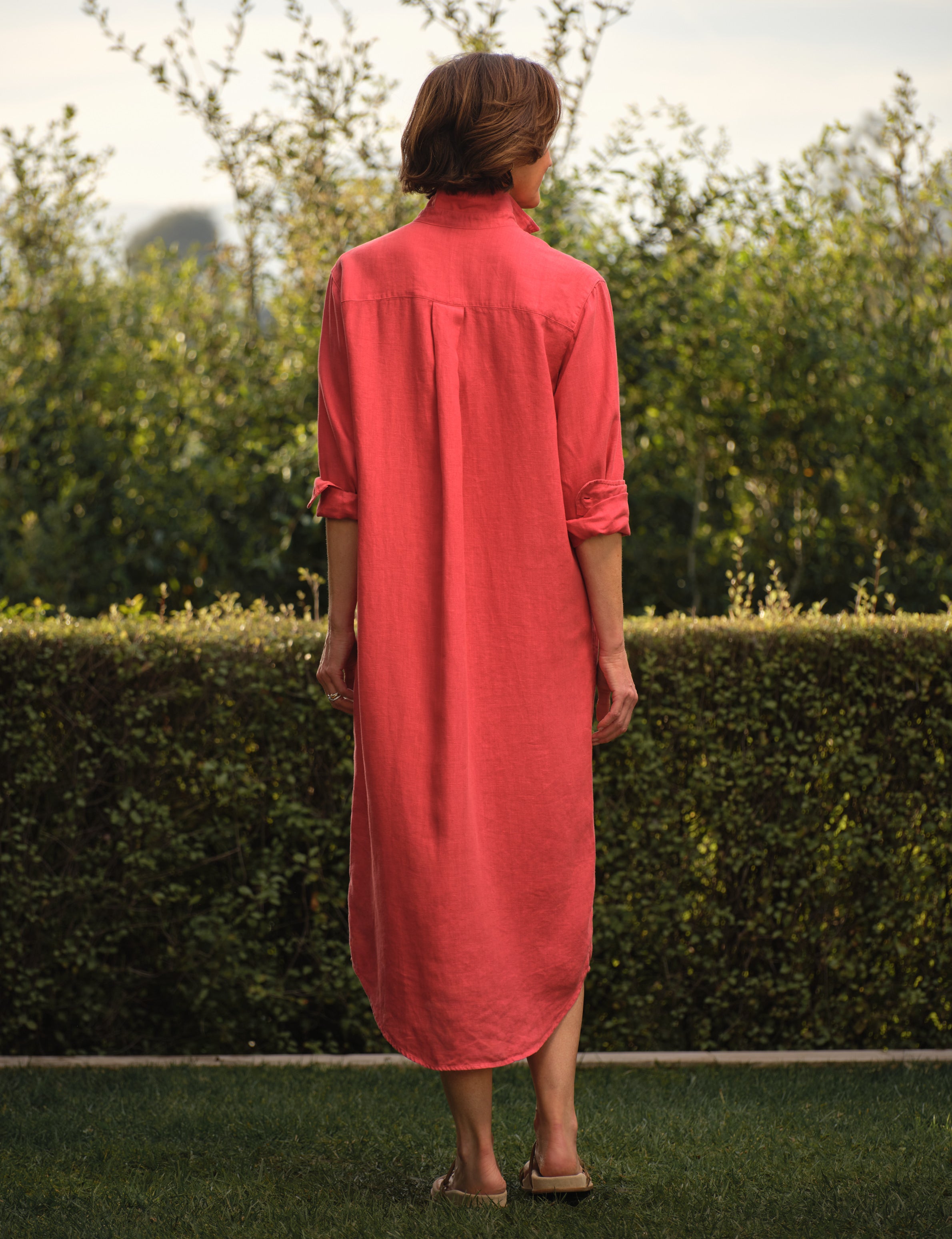 Person wearing a red dress standing in a garden, alternate view